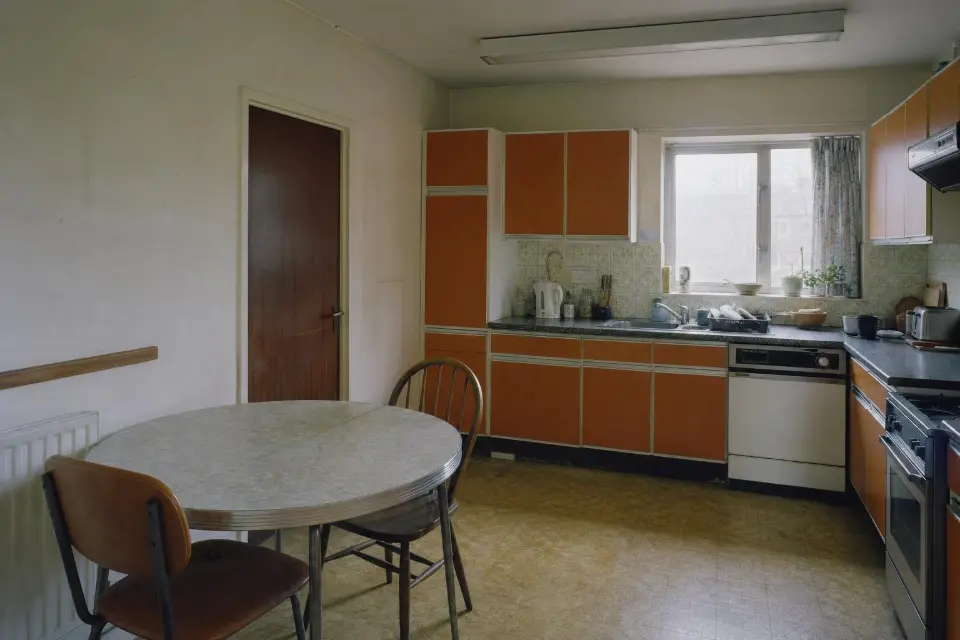 A dated 1980s kitchen with orange-brown laminate cabinet fronts and a patterned tile splashback.